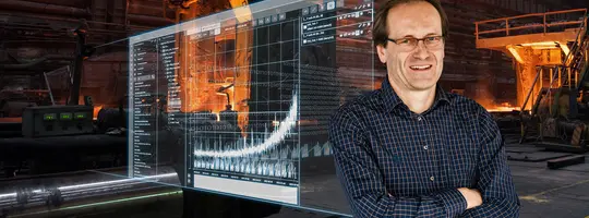 A man in a plaid shirt and glasses smiles in a dark factory, with a transparent digital overlay showing data graphs.