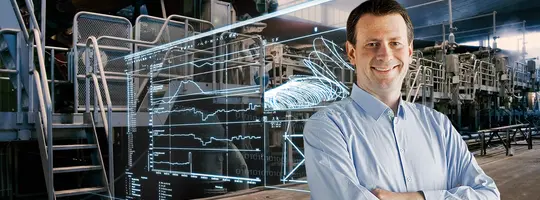 A smiling man in a light blue shirt with crossed arms stands in a factory, overlaid by a transparent digital interface.